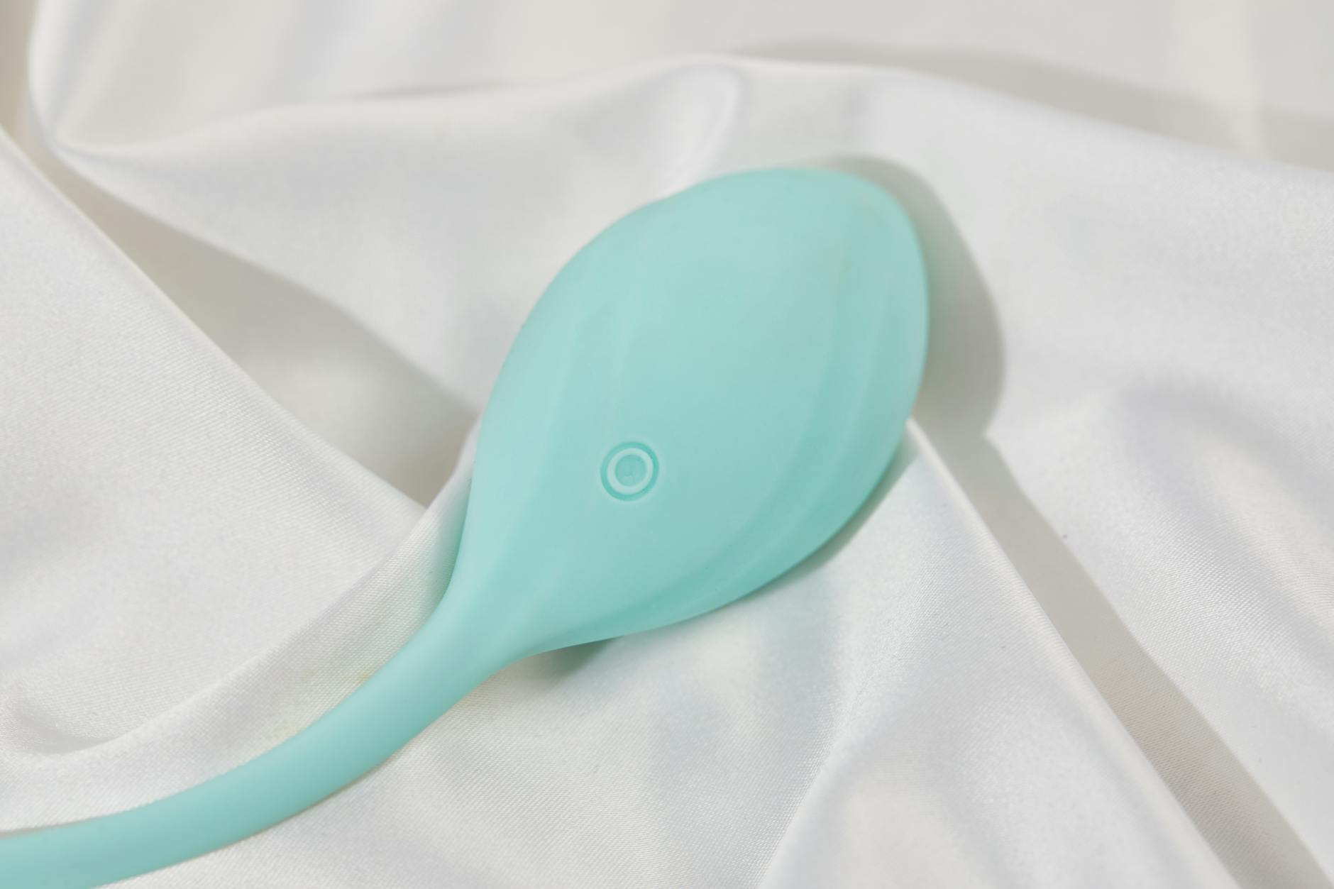 A teal lemon vibrator resting on white silk fabric