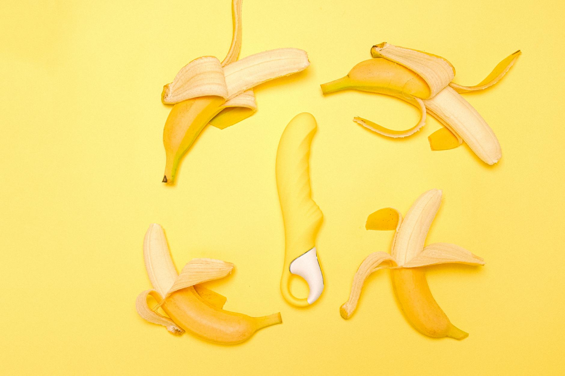 Vibrador de silicone amarelo circundado por arranjo criativo em fundo amarelo brilhante.