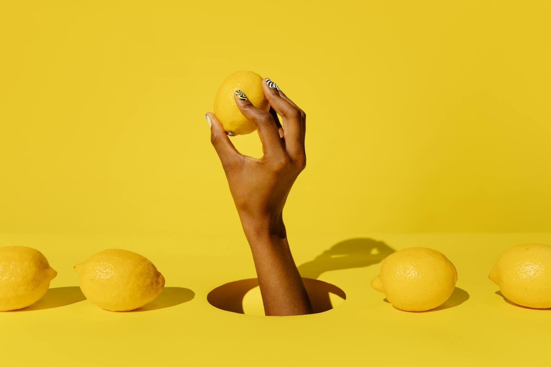 A hand holding a fresh lemon against a bright yellow background, symbolizing natural wellness and refreshment