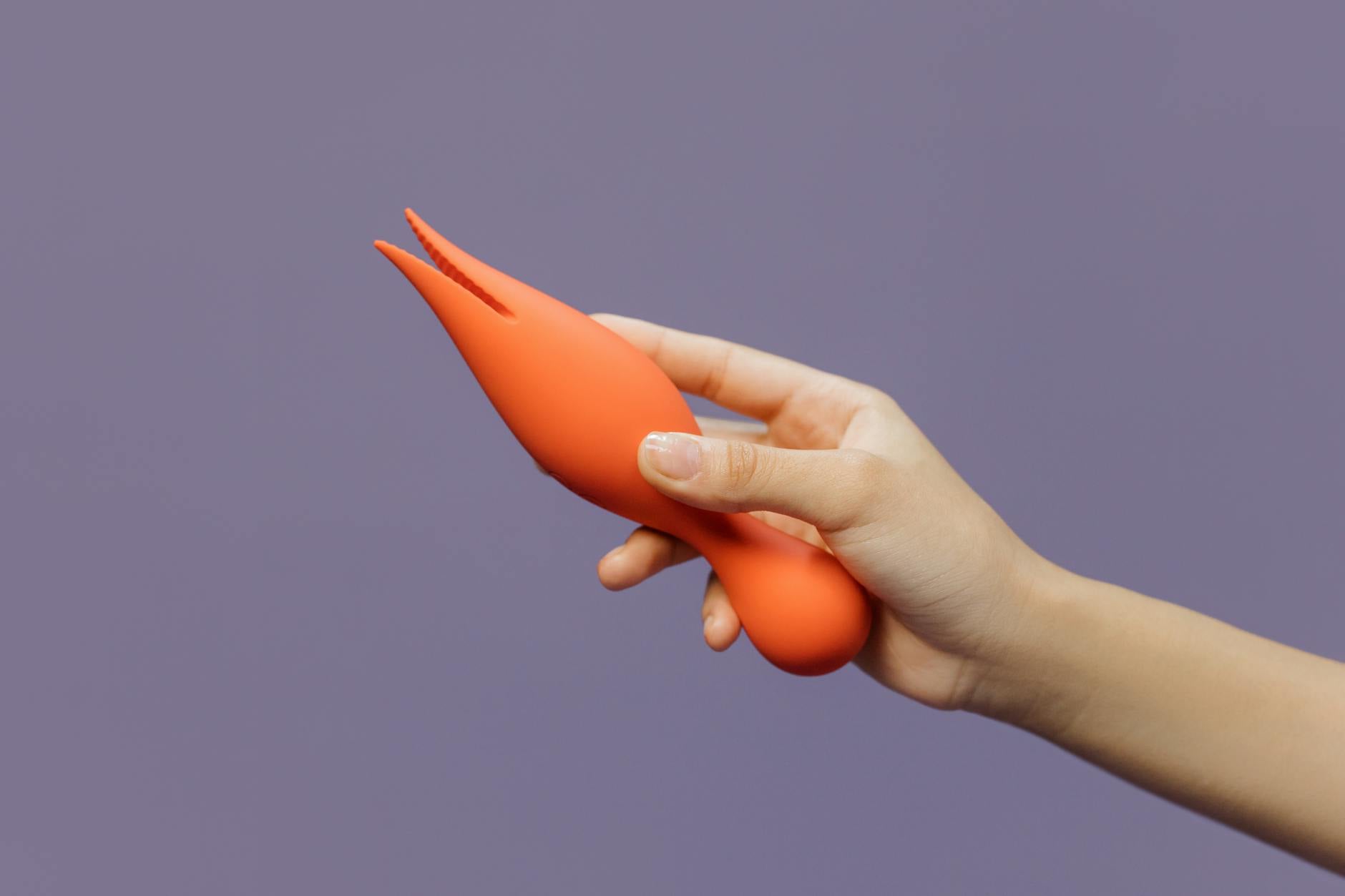Close-up of a hand holding The Lem vibrator against a minimalist purple backdrop