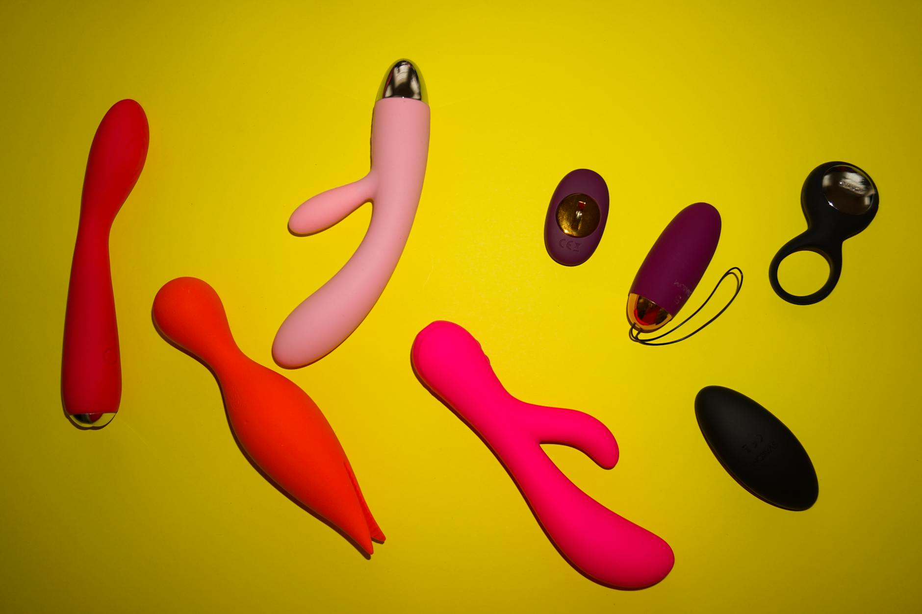 Vibrant collection of various clitoral vibrators arranged on a bright yellow surface, showcasing diverse designs and finishes.