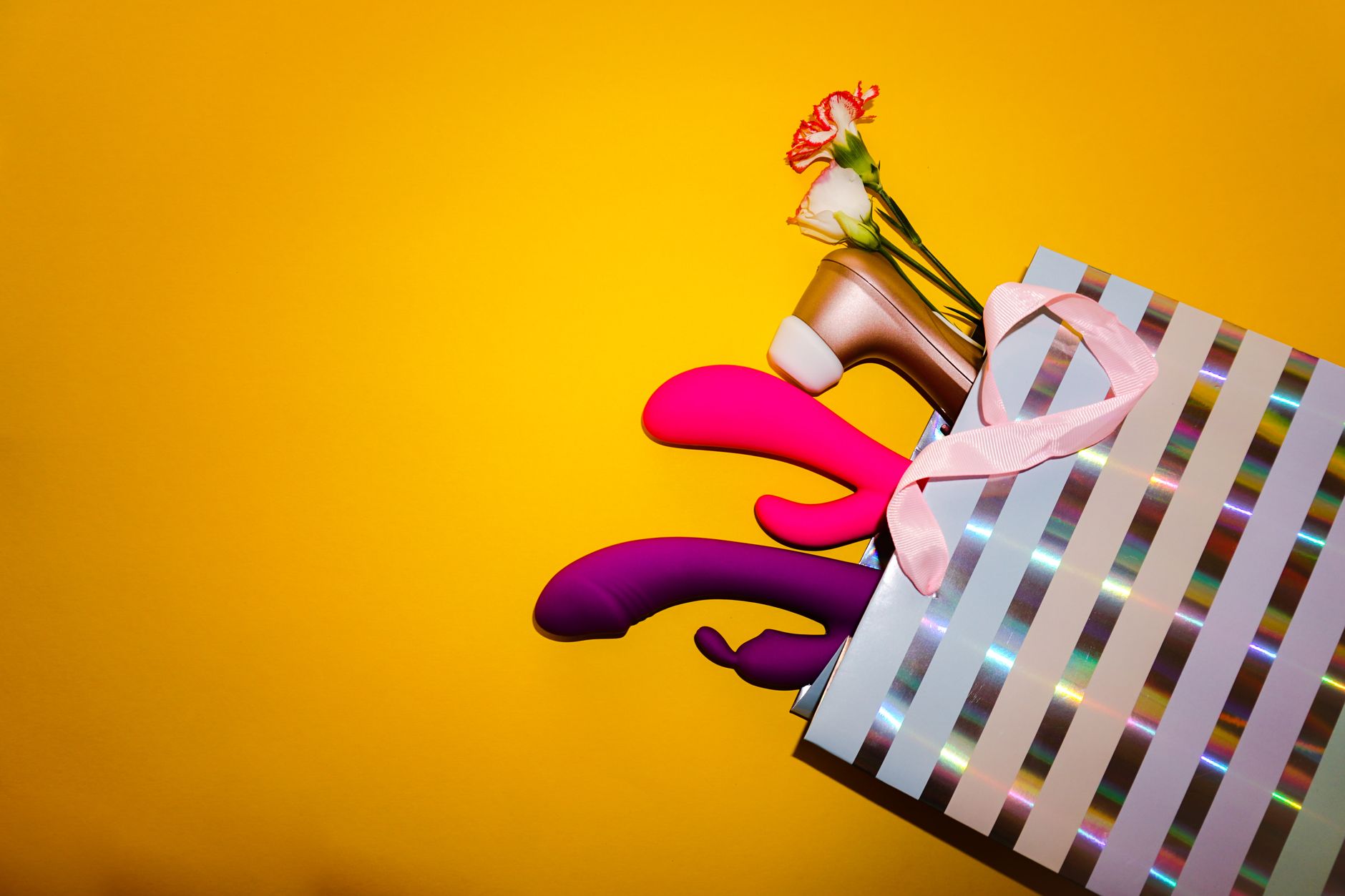 Colorful lemon vibrators and clitoral toys arranged with flowers against a bright yellow background