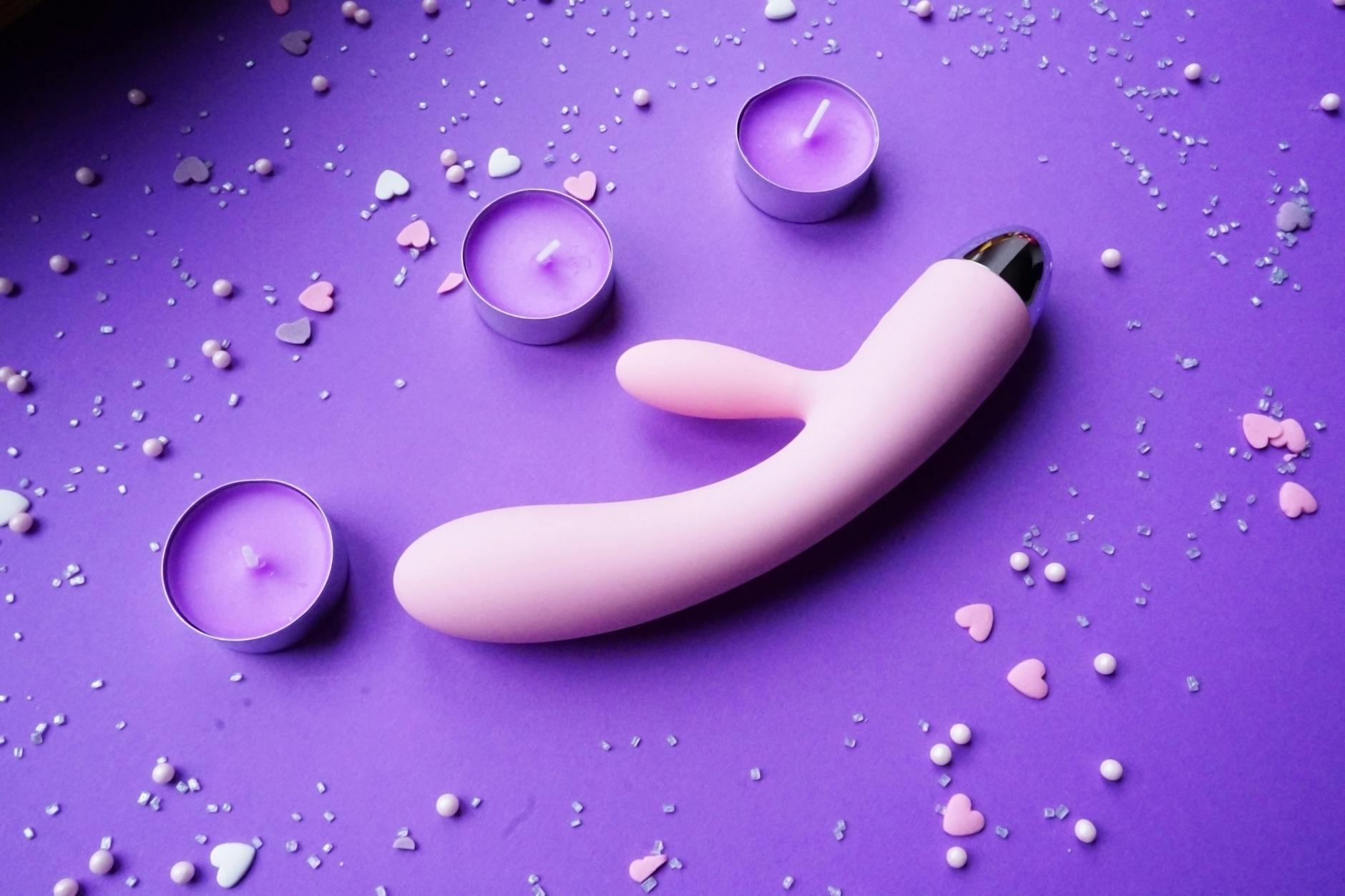 Pink lemon vibrator on purple background with candles and heart confetti symbolizing romantic couples exploration