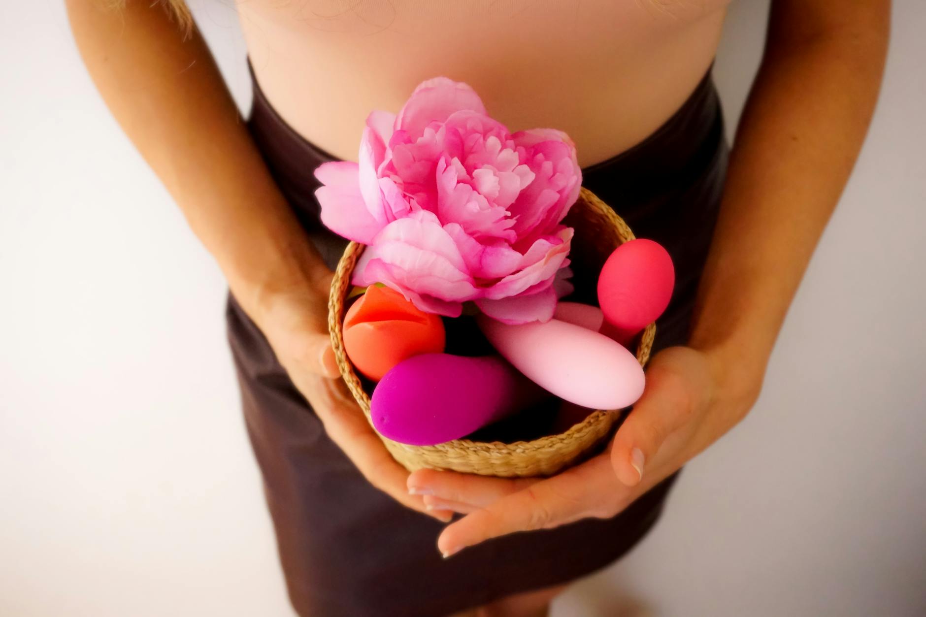 Two hands holding vibrators against a pastel background